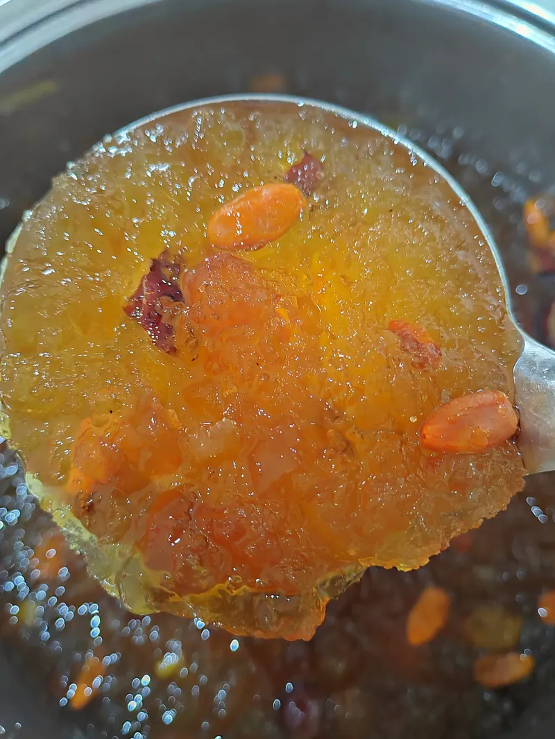 锅里刚煮好的桃胶雪燕，大汤勺捞起一勺金黄透亮的桃胶，看得到红枣和枸杞。