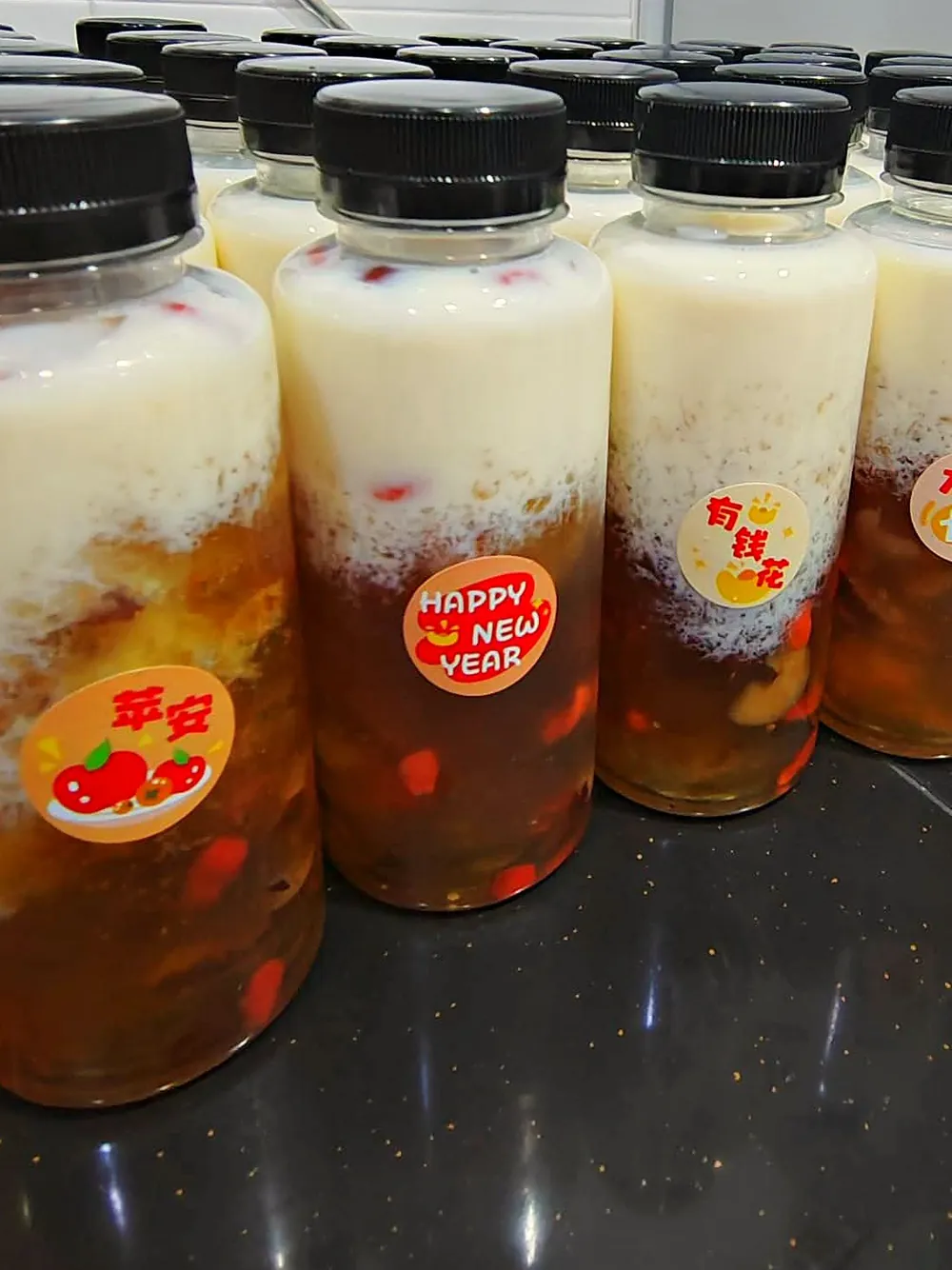 一排桃胶雪燕牛奶，前面三瓶贴着平安、Happy New Year、有钱花的祝福贴纸。