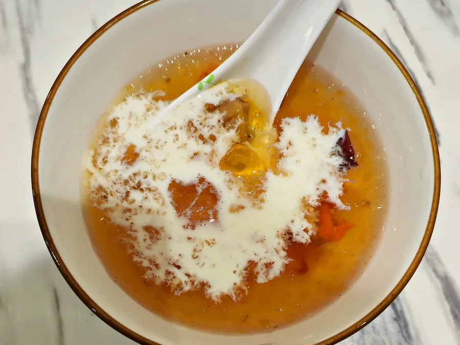 白碗里的桃胶雪燕牛奶，牛奶刚淋在金黄的桃胶上，白色汤匙放在碗里，俯拍。